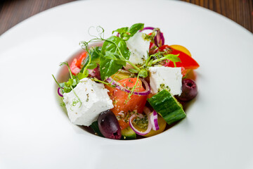 Greek salad with feta on white plate on wooden table