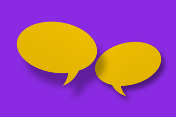 Speech balloon shaped yellow paper against purple background.