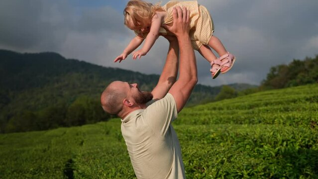 father is holding his cute little daughter on hands and lifting up, kissing tenderly