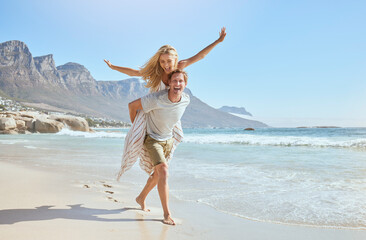 Portrait of a happy and loving young couple enjoying a day at beach in summer. Cheerful affectionate husband giving his joyful wife a piggyback while walking and having fun by the seashore on holiday