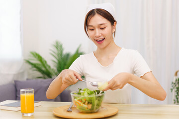 Obraz na płótnie Canvas Lifestyle in living room concept, Asian woman using spoon to ladle salad dressing into salad bowl