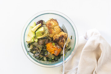 High angle closeup of vegetarian meal in glass bowl with beige napkin including avocado, roasted cauliflower and stir fried greens (selective focus)