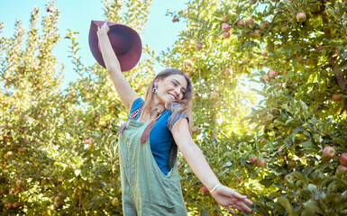 Excited young woman jumping for joy in an apple orchard on a sunny day outside. Happy and cheerful farmer feeling optimistic, free and full of energy after a fruitful harvest on her successful farm