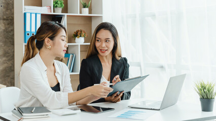 Two Asian female office workers working together with laptop at the white working desk in the comfortable meeting room.