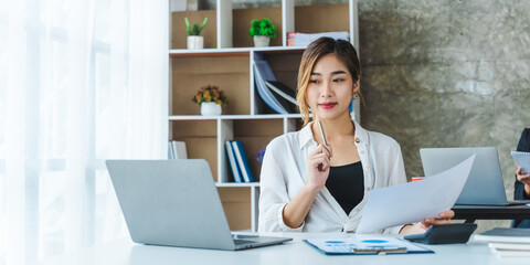 Business asian woman using laptop for do math finance on wooden desk in office, tax, accounting, financial concept