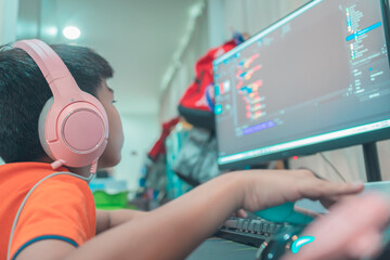 Asian kid is coding and scripting program on on his game streaming desktop computer with headphone on.
