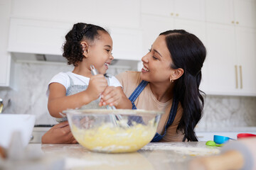 Happy mixed race mother and daughter baking and bonding. Young woman helping her daughter bake at...