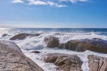 A rocky shore and a view of the ocean with waves, blue sky copy space, and a horizon in the background in Camps Bay, Cape Town, South Africa. Calm, serene, tranquil beach and nature scenery