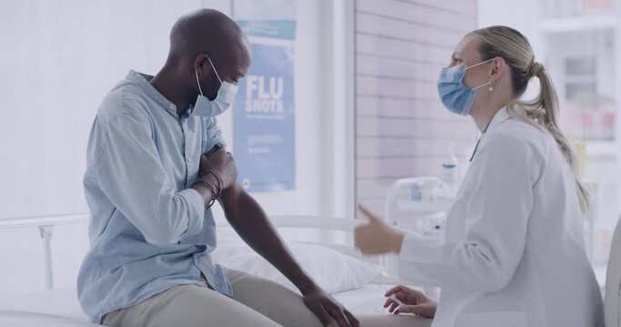 Female doctor injecting syringe with covid vaccine in arm of a male patient while wearing masks. Healthcare worker giving a patient thumbs up after receiving coronavirus immunization in a clinic