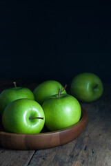 Delicious green apples are placed in a wooden tray and rest on a rustic wooden floor.