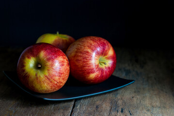 Delicious red apples are placed on a black square ceramic plate on a rustic wooden floor.