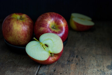 Delicious red apples, whole, and halves put on a black ceramic tray on a rustic wooden floor.