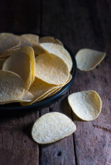 Potato chips in a black ceramic tray on a rustic wooden floor.