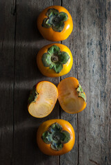 Slice and whole persimmons on a rustic wooden background.