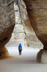 person walking with typical Arab clothes inside a canyon among the rocks of the mountains of the desert