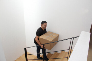 Latino adult man carries a heavy cardboard box up stairs which causes severe pain in his lower back...