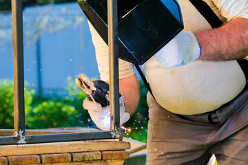 Male welder welds metal pipes on the table. The master works with electric arc welding.