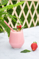 Strawberry smoothie or milkshake with banana and mint in a glass glass on a table in the garden. Refreshing organic vegan summer drink. Clean eating.
