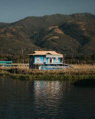 Burmese style blue wooden house on Inle Lake in Myanmar on a sunny day with mountains in the background. 