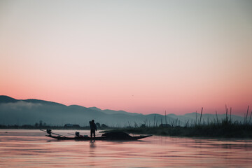 Beautiful colorful sunrise on Inle Lake in Myanmar with a local boat on the water.