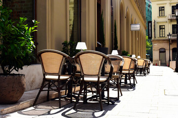 open street or sidewalk terrace of restaurant in European urban setting. chairs and tables. decorative green plants. summer scene. table lamps. travel and tourism concept. diminishing perspective.
