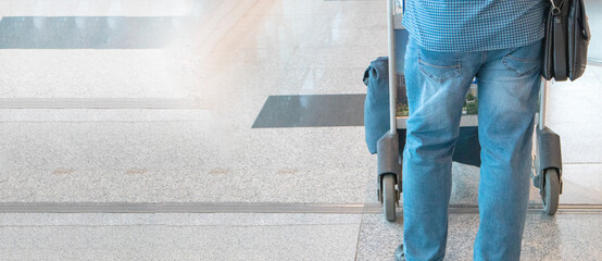 Banner a male passenger in blue jeans and a shirt, pushing a trolley with luggage at the airport, a view from the back, a copy of the space on the left