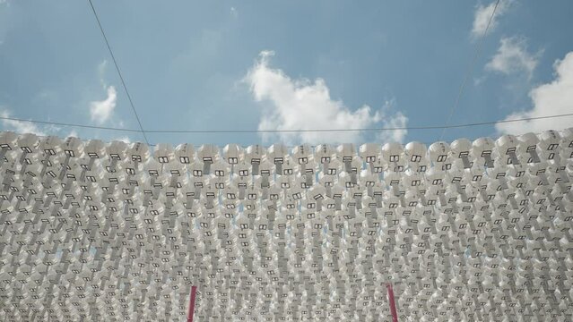 Rows of White Color Rounded Pater Lanterns with Blessing Cards Hanging on Lines for Decoration Against Blue Sky in Buddhist Temple