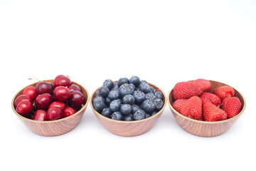 Blueberries, strawberries and cherry in bowls on white background