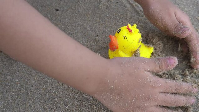 Little kid hand play sand and rubber duck toy at beach