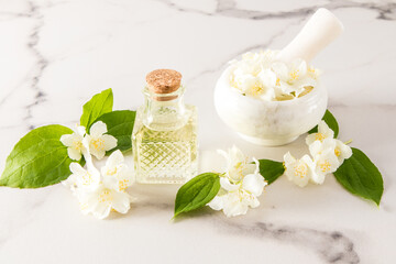Fototapeta na wymiar glass vial with organic jasmine oil, mortar and pistil with flowers on a marble white background. the concept of natural oils.
