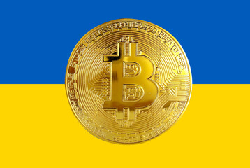 Holds a physical version of Bitcoin and the Ukrainian flag. Conceptual image of Ukraine's...