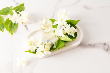 Obraz na płótnie Canvas open cosmetic bottle with an organic natural product based on jasmine oil on a white plaster tray with flowers. alternative to medicine.