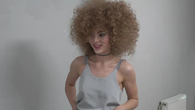 European girl blonde hairstyle afro curls cool posing against wall background.