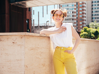 Young beautiful smiling hipster woman in trendy summer yellow jeans clothes. Carefree teen model posing in the street at sunset. Positive female outdoors. Cheerful and happy. In sunglasses