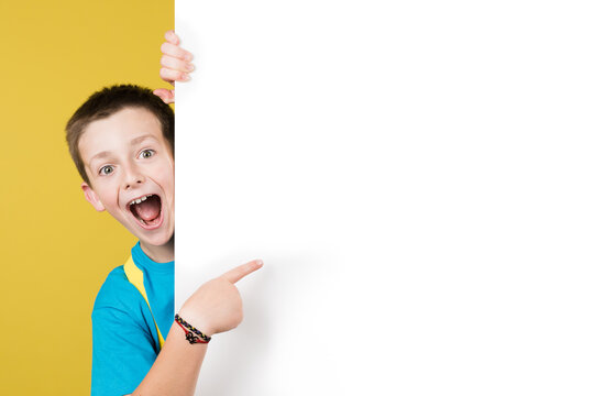 Amazed boy pointing at white billboard at side. Back to school advertising or message concept. Schoolboy showing copy space