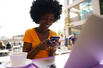 Happy afro woman using mobile phone at outdoor cafe