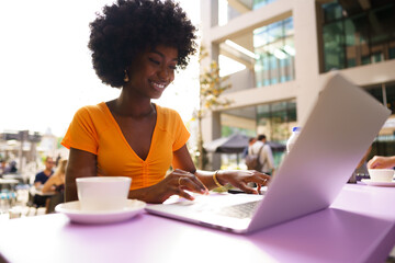 Happy beautiful young black woman using laptop in cafe