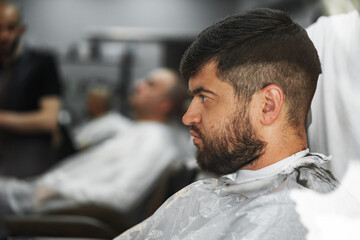 Male client getting haircut by hairdresser in barbershop