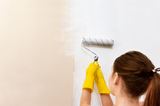 home repairs, painting walls with paint, renovation,
girl child in yellow gloves paints a wall with a roller with white paint