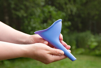 Device for women, pee funnel, to use while camping outdoors, helps urinating standing. Woman hands holding the tool. - obrazy, fototapety, plakaty