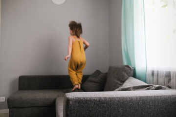 Cute girl child one gallops on couch in living room
