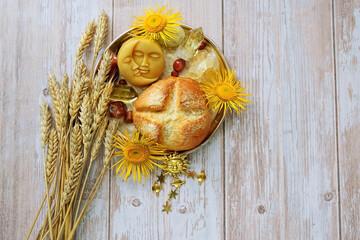 ears of wheat, bread, sun and moon amulet, gemstones, flowers on wooden table. altar for Lammas,...