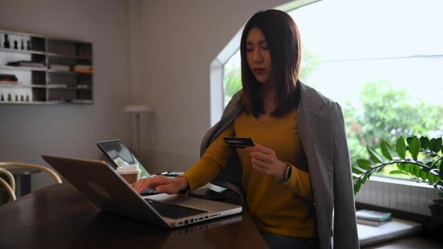 Asian woman hand using smart phone, tablet payments and holding credit card online shopping, omni channel, digital tablet docking keyboard computer at office