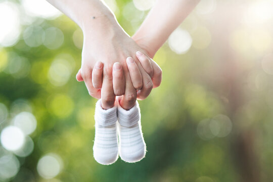 Future Parents Holding Hands And A Pair Of Newborn Baby Shoes With Isolated Blur Garden Background