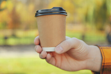 Male hand holding blank paper cup outdoor, close up