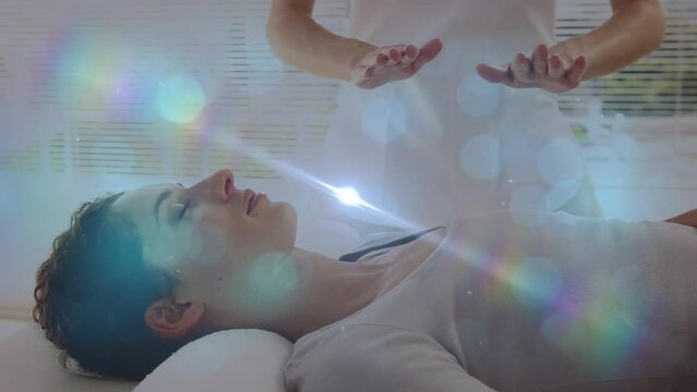 Animation of lights over caucasian woman healing with hands female patient