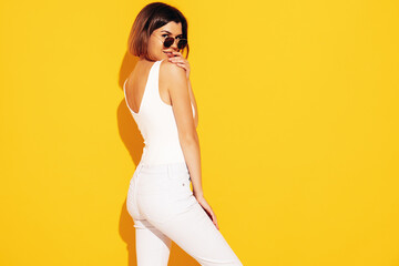 Young beautiful smiling female in trendy summer white jeans clothes. Carefree woman posing near yellow wall in studio. Sexy positive model having fun indoors. Cheerful and happy