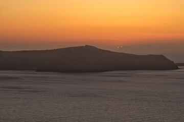 View of the sun slowly setting behind the volcano of Santorini and producing a spectacular sunset