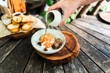 A man pours pesto into a dish of pulled beef. Stylish lunch on a wooden table