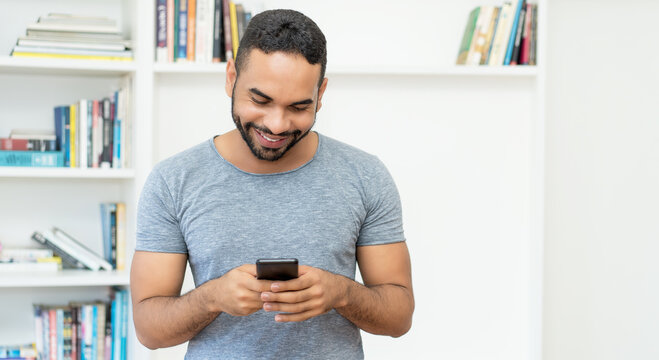 Laughing hispanic hipster man with beard sending message at mobile phone